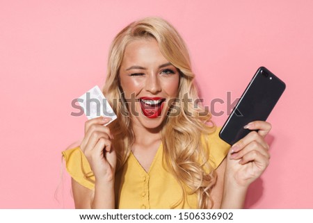 Image of caucasian woman with long blond hair smiling while holding cellphone and credit card isolated over pink background