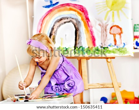 Little girl painting at easel in school. Education.