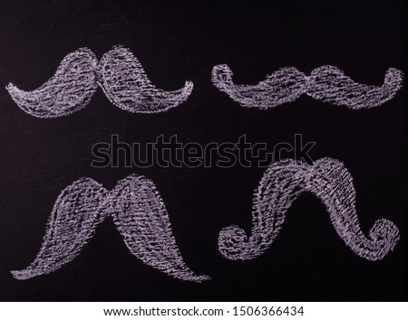 Chalk-painted mustaches on a black school board, copy space. Top view.
