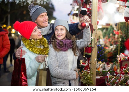 admiring family couple with teen daughter choosing Christmas decoration at fair