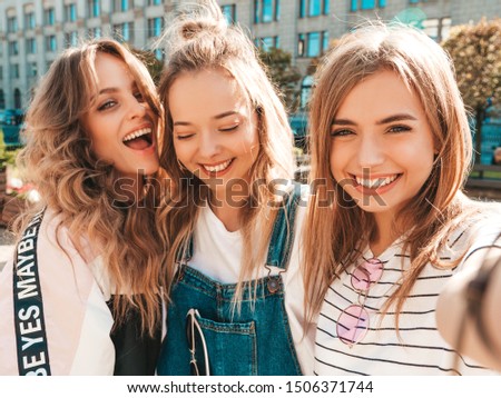Three young smiling hipster women in summer clothes.Girls taking selfie self portrait photos on smartphone.Models posing in the street.Female showing positive face emotions 