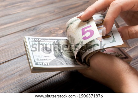 Perspective view of female hands counting money. One hundred and five dollar banknotes on wooden background. Salary concept. Bribe concept.