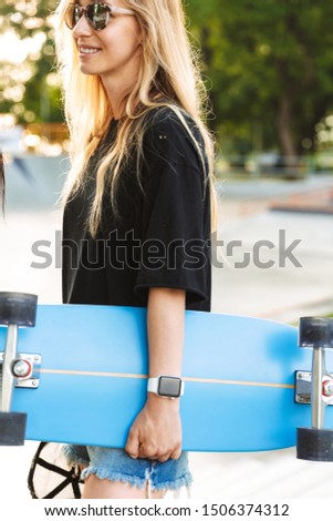 Attractive funky teenage girl carrying longboard while walking at the skatepark