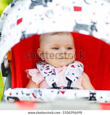 Cute little beautiful baby girl of 6 months sitting in the pram or stroller and waiting for mom. Happy smiling child with blue eyes.