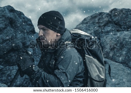tired hiker with trekking poles and hiking rucksack breathe out in front of rocky landscape