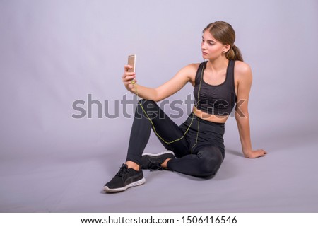 Portrait of young woman listening to music using earphones and smartphone in studio on gray background. Sport girl, fitness.