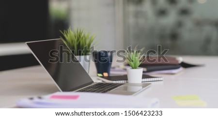 Open laptop computer with office supplies and documents on white table in modern office style 