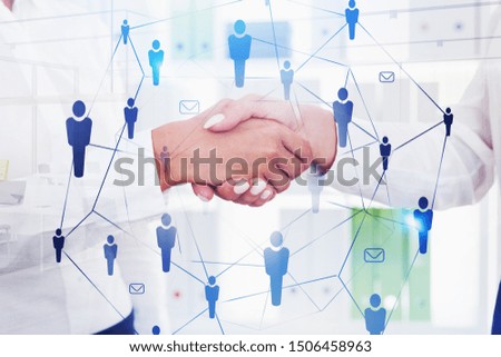 Two businesswomen shaking hands in blurred office with double exposure of social network interface. Concept of partnership and communication. Toned image