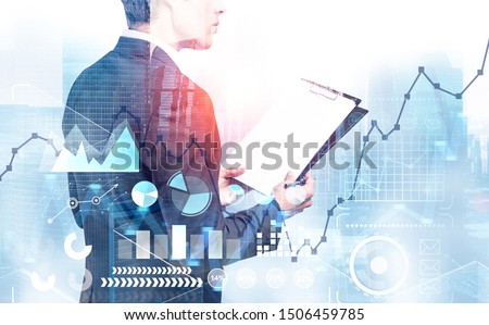 Unrecognizable young CEO with clipboard working in modern city with double exposure of business infographics and HUD interface. Concept of statistics and data. Toned image