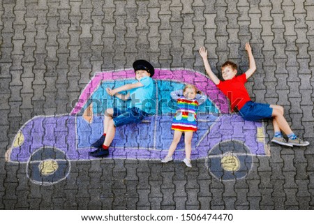 three little children, two school kids boys and toddler girl having fun with with car picture drawing with colorful chalks on asphalt. Siblings painting on ground playing together. Creative leisure