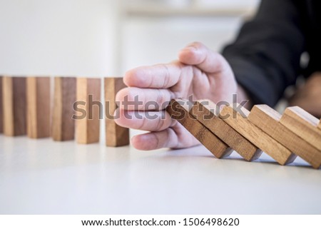 Risk and Strategy in Business, Image of hand stopping falling collapse wooden block dominoes effect from continuous toppled block, prevention and development to stability. Royalty-Free Stock Photo #1506498620