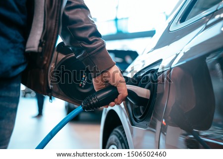 Human hand is holding Electric Car Charging connect to Electric car Royalty-Free Stock Photo #1506502460