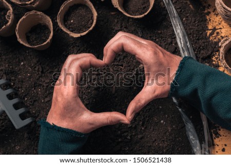 Gardener hand heart gesture over the table with organic gardening and farming equipment, close up of female hands