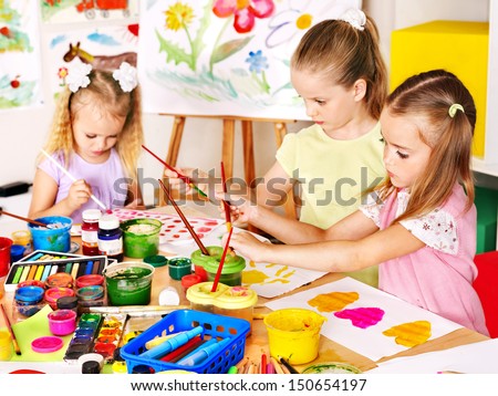 Child painting at easel in school. Teacher help.