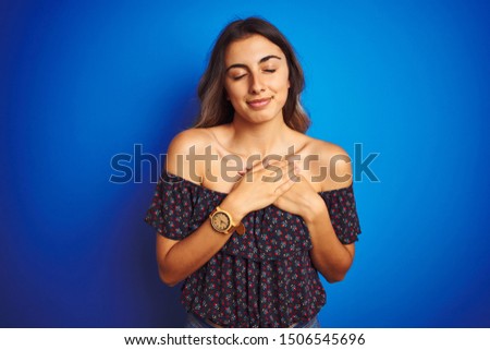 Young beautiful woman wearing floral t-shirt over blue isolated background smiling with hands on chest with closed eyes and grateful gesture on face. Health concept.