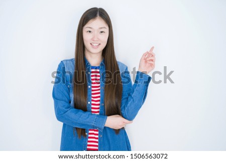 Beautiful young asian woman over white isolated background with a big smile on face, pointing with hand and finger to the side looking at the camera.