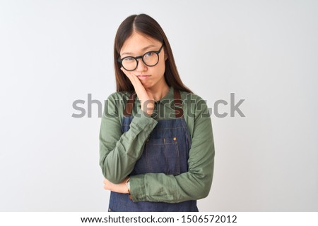 Young chinese shopkeeper woman wearing apron and glasses over isolated white background thinking looking tired and bored with depression problems with crossed arms.