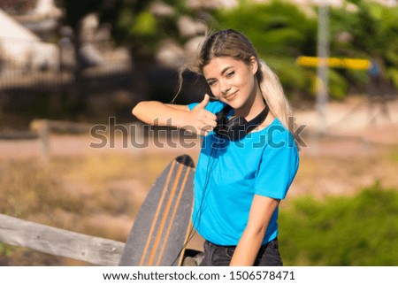 Teenager girl with skate at outdoors with thumbs up because something good has happened