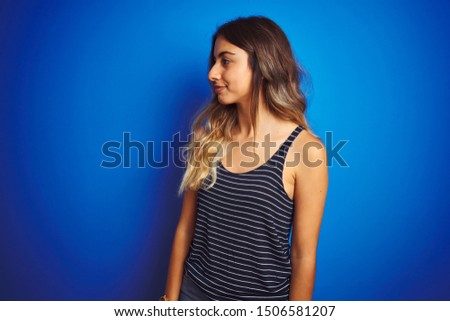 Young beautiful woman wearing stripes t-shirt over blue isolated background looking to side, relax profile pose with natural face with confident smile.