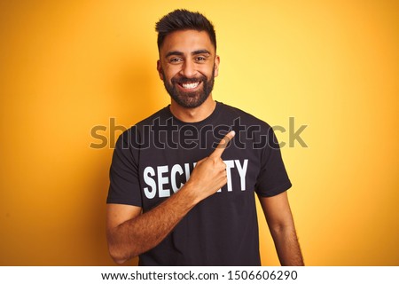 Arab indian hispanic safeguard man wearing security uniform over isolated yellow background cheerful with a smile of face pointing with hand and finger up to the side with happy and natural expression