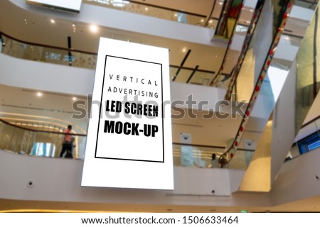 Mock up large blank vertical LED screen hanging from ceiling between floors near escalator with clipping path in shopping mall, empty space for insert media or information promotion