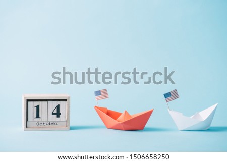 wooden calendar with October 14 date near paper boats with American flag pattern on blue background 