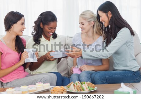 Friends offering gifts to dark woman during party at home on couch