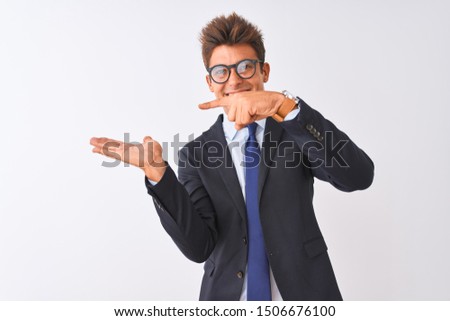 Young handsome businessman wearing suit and glasses over isolated white background amazed and smiling to the camera while presenting with hand and pointing with finger.