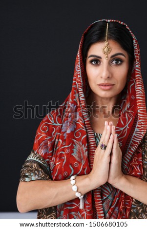 Image of gorgeous hindus girl in traditional indian saree dress and jewelry dancing with palms together isolated over black background