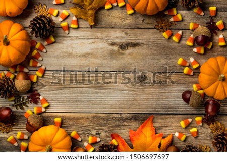 Top down view of a variety of autumn decorations forming a border against a wooden background and copy space in the middle.
