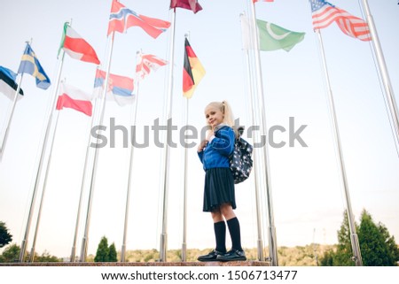 Little schoolgirl with school backpack on background of flags of foreign countries. Back to school.