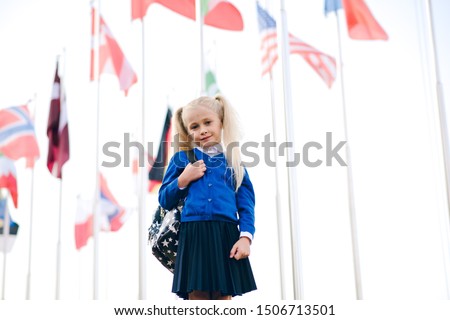 Little schoolgirl with school backpack on background of flags of foreign countries. Back to school.