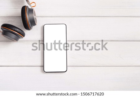 Listen music online. Closeup of smartphone with blank screen and modern headphones on white wooden background, copy space