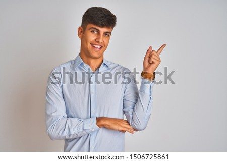 Young indian businessman wearing elegant shirt standing over isolated white background with a big smile on face, pointing with hand and finger to the side looking at the camera.