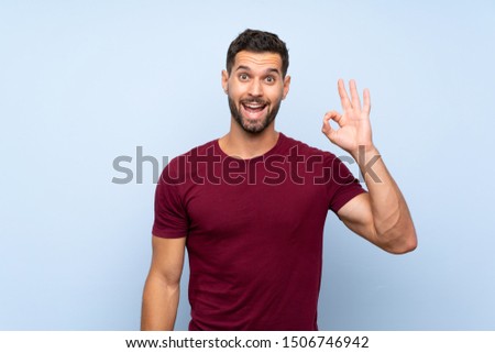 Handsome man over isolated blue background surprised and showing ok sign