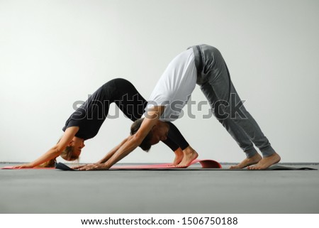 A young slender girl and a young man do yoga. They stand on a yoga mat in a dog pose face down.