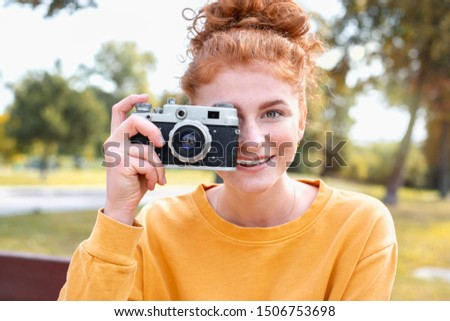Smiling happy red hair student girl taking picture with old vintage camera outside in autumn park. Study students conceprt.