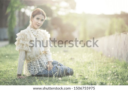Asian woman bride in thai traditional costume sit on grass at outdoor in a morning surrounding by golden sunlight and grass flower.
