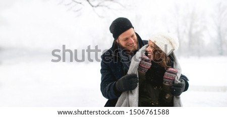 Young man hugging young women with blanket on a snowy day