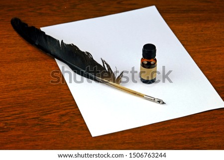 Calligraphy feather quill dip pen on white paper placed on wooden table.