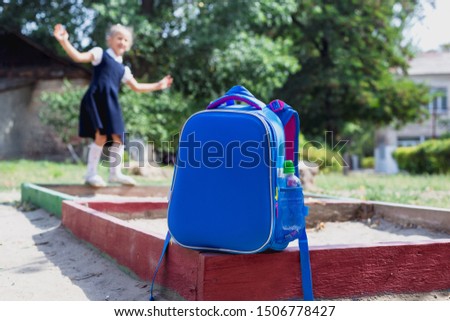 Back to school concept. A school backpack in the foreground and a junior schoolgirl on the playground in the background. Accent photos on a school backpack.