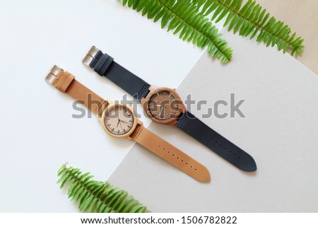 Top view of 2 wooden watches on white and brown color background. Nature leafs and leather band watch on soft color background.
