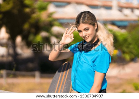 Teenager girl with skate at outdoors showing ok sign with fingers