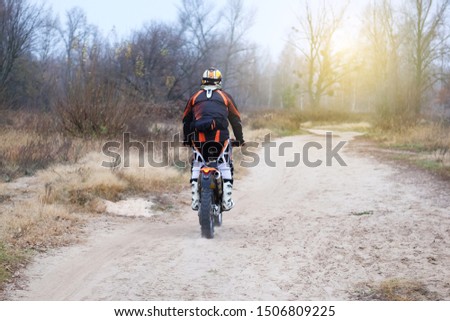 Sport and active healthy life concept. Motorcyclist in protective late fall forest. Riding on motorcycle on sunny day among many trees.