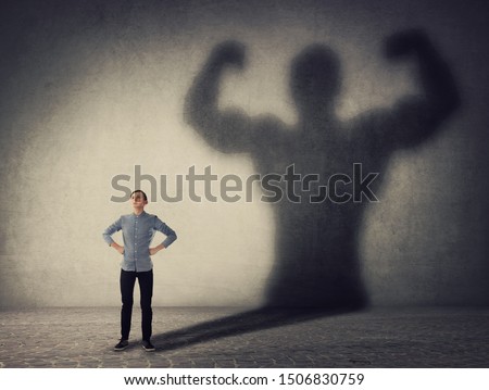 Brave teenager boy facing his fears as a powerful hero. Guy casting a strong muscular bodybuilder shadow, showing big biceps. Self defense, inner strength and motivation and confidence concept. Royalty-Free Stock Photo #1506830759