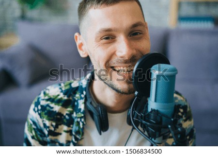 Portrait of joyful guy hipster talking in microphone in recording studio smiling looking at camera wearing casual clothing. People, equipment and occupation concept.