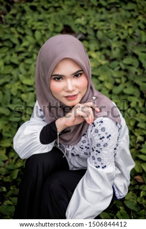 Beautiful  moslem woman wearing hijab  sitting on the green grass with blured background .