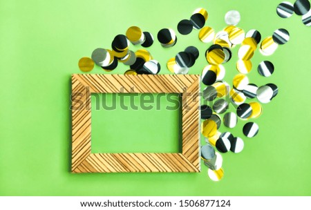 Shiny golden, silver and black confetti and light wooden frame on yellow green background. Festive modern concept.