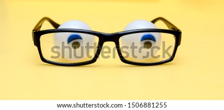 Black frame of glasses on a yellow background. Behind the glasses are tennis balls with glued pupils. Concept - eyes behind the glasses of glasses, expressing fear, confusion, thoughtfulness. 