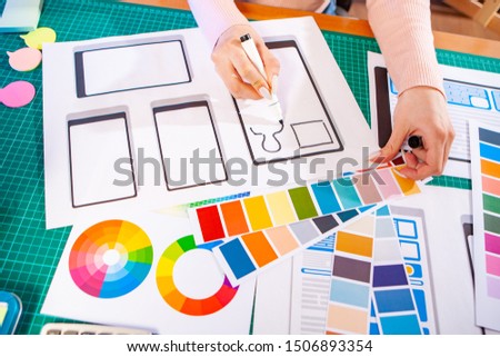 Desktop of mobile application designer. Development of a new user interface programs. Girl draws a sketch of the screen. Choice of color scheme.